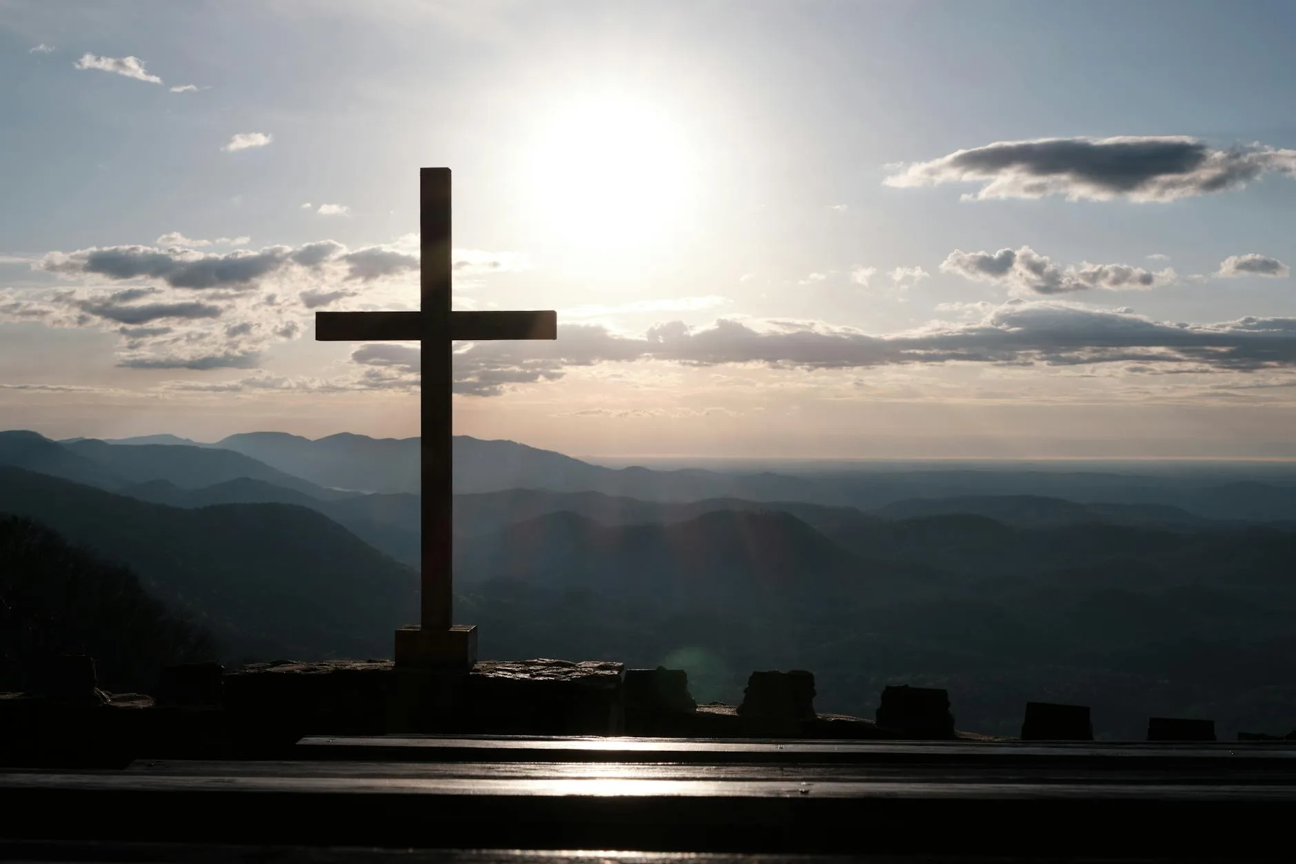 Wooden cross silhouetted against a sunset over mountain ranges
